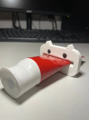 Exprimidor blanco con orejitas apretando un pomo de pasta dental